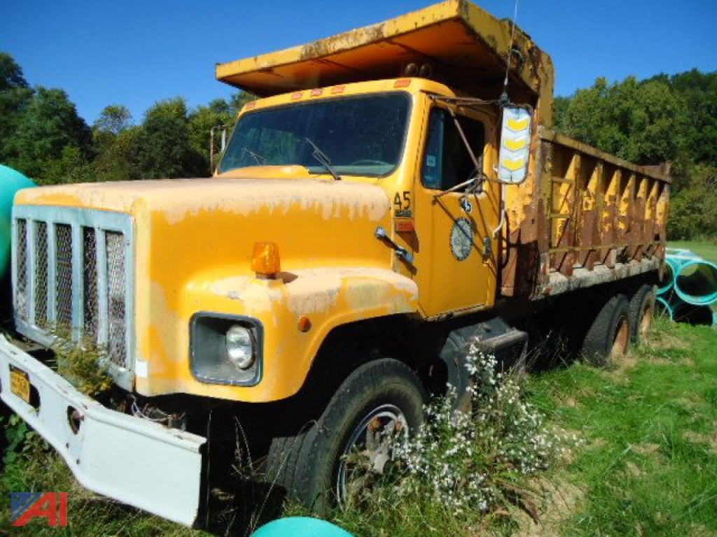 International dump truck with yellow cab and dump body in an open field showing worn paint and grass around wheels.