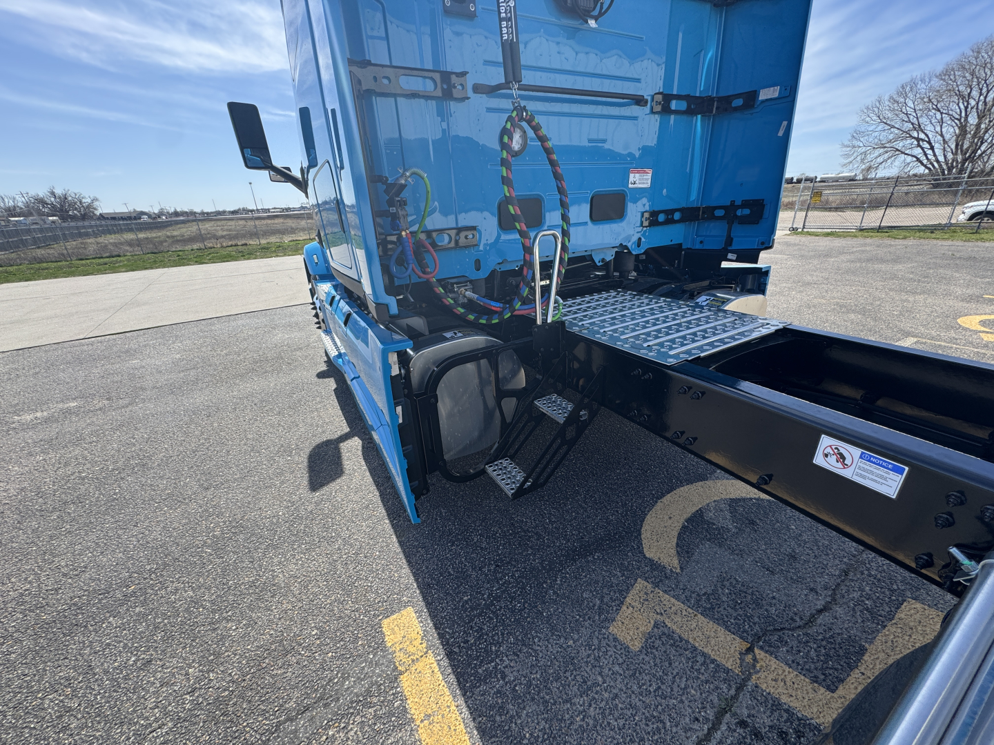 Truck chassis and blue sleeper cab side view showing rear access steps, tow hooks, and wiring harness near fifth wheel area.