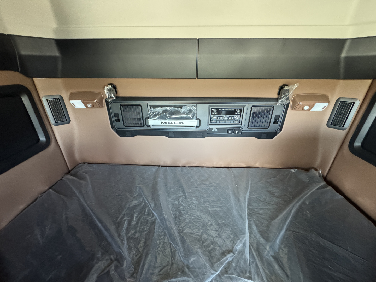 Dashboard area of a Mack truck sleeper cab showing control panels and logo plate in the center console.