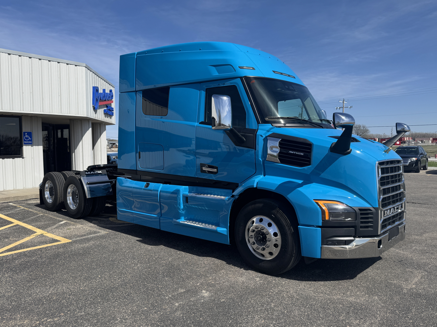 Blue Mack AN64T64 sleeper cab truck parked in front of a dealership, front and side views visible with chrome bumper and dual rear axles.