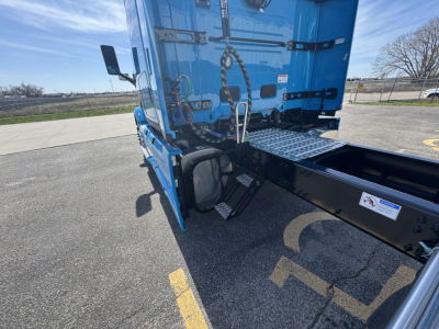 Truck chassis and blue sleeper cab side view showing rear access steps, tow hooks, and wiring harness near fifth wheel area.