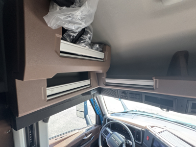 Truck cab interior showing dashboard and steering wheel from a Mack AN64T64 sleeper cab, with overhead sleeper area and passenger window visible.