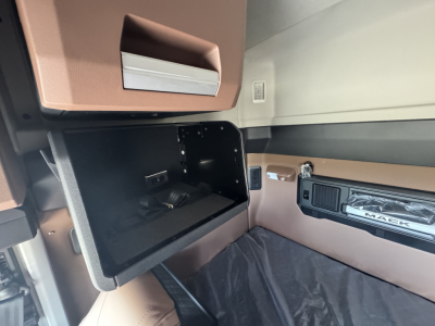 Truck cab interior showing open overhead storage compartment and dashboard with Mack branding and tan/brown trim.
