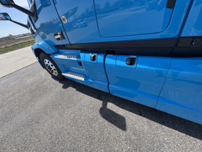 Truck side view showing blue Mack AN64T64 with metallic steps and door area; visible text includes part of the cab and wheel.