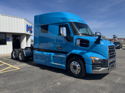 Blue Mack AN64T64 sleeper cab truck parked in front of a dealership, front and side views visible with chrome bumper and dual rear axles.