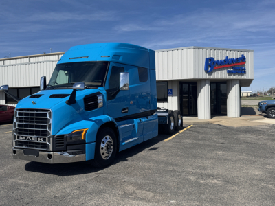 Blue Mack AN64T64 sleeper cab truck in front of dealership building with Mack grille and chrome bumper.