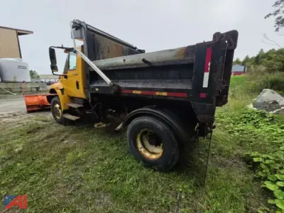 Dump truck bed with plow and wing attachments on a yellow International 4300 dump truck, side view, in grassy lot.
