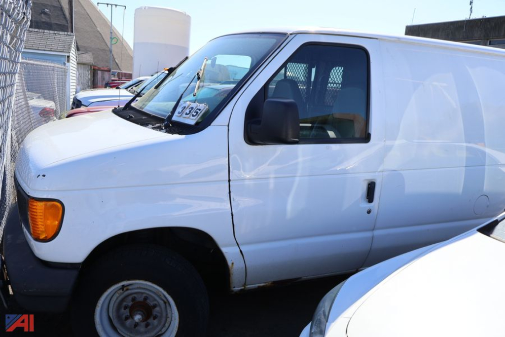 Ford E-250 cargo van side view showing front door and wheel, white exterior, black mirror, windshield with price tag.