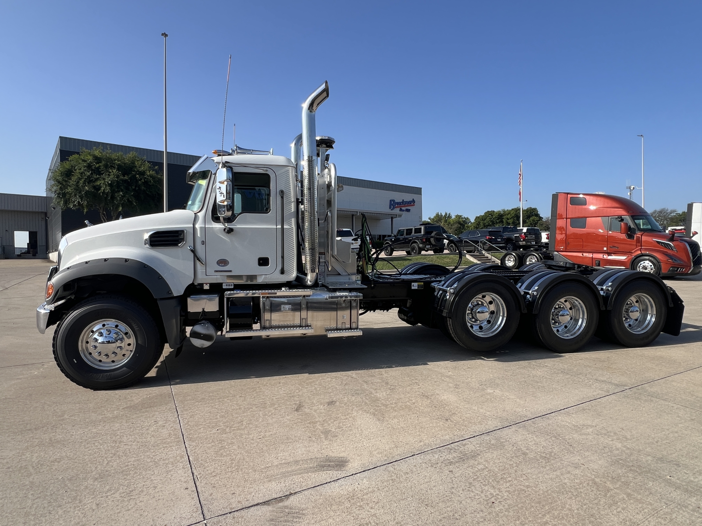 Side view of a white 2027 Mack GR84FT conventional daycab tractor with chrome exhaust stacks and dual rear axles, empty trailer space, clear sky.