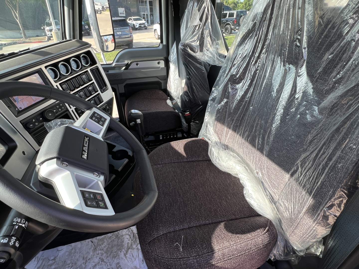 Mack GR84FT truck cab interior showing steering wheel, instrument cluster, and driver seat with plastic covering; dashboard with gauges and controls visible.