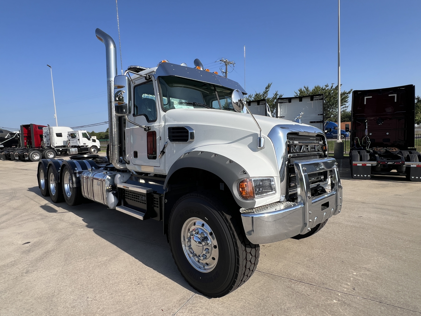 Truck cab of a 2027 Mack GR84FT conventional daycab showing chrome bumper, large exhaust stack, dual rear axles, and front grille with Mack emblem.