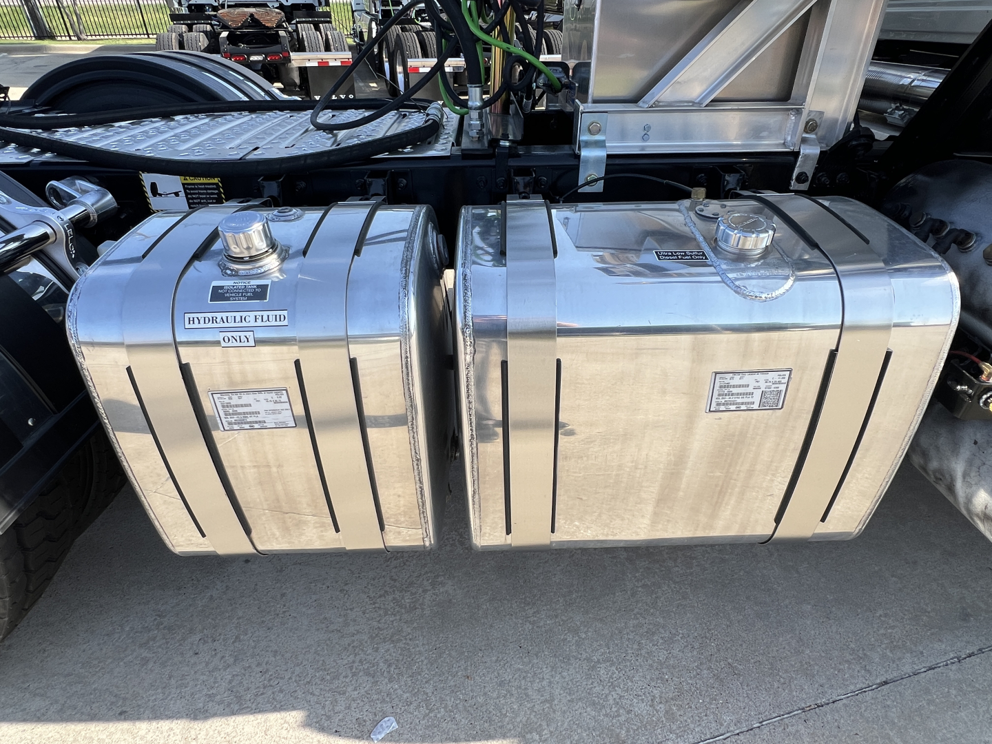 Dual polished aluminum fuel tanks mounted on Mack GR84FT truck chassis with hoses and mounting brackets visible above.