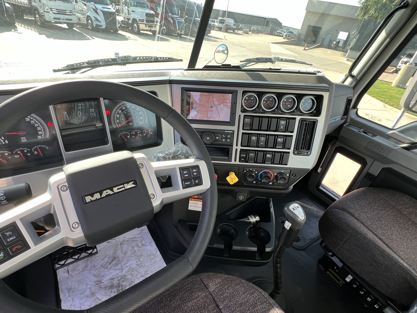 Mack GR84FT truck interior cockpit showing steering wheel with MAC logo, instrument cluster, multi-gauge panel, climate controls, and gear shifter.