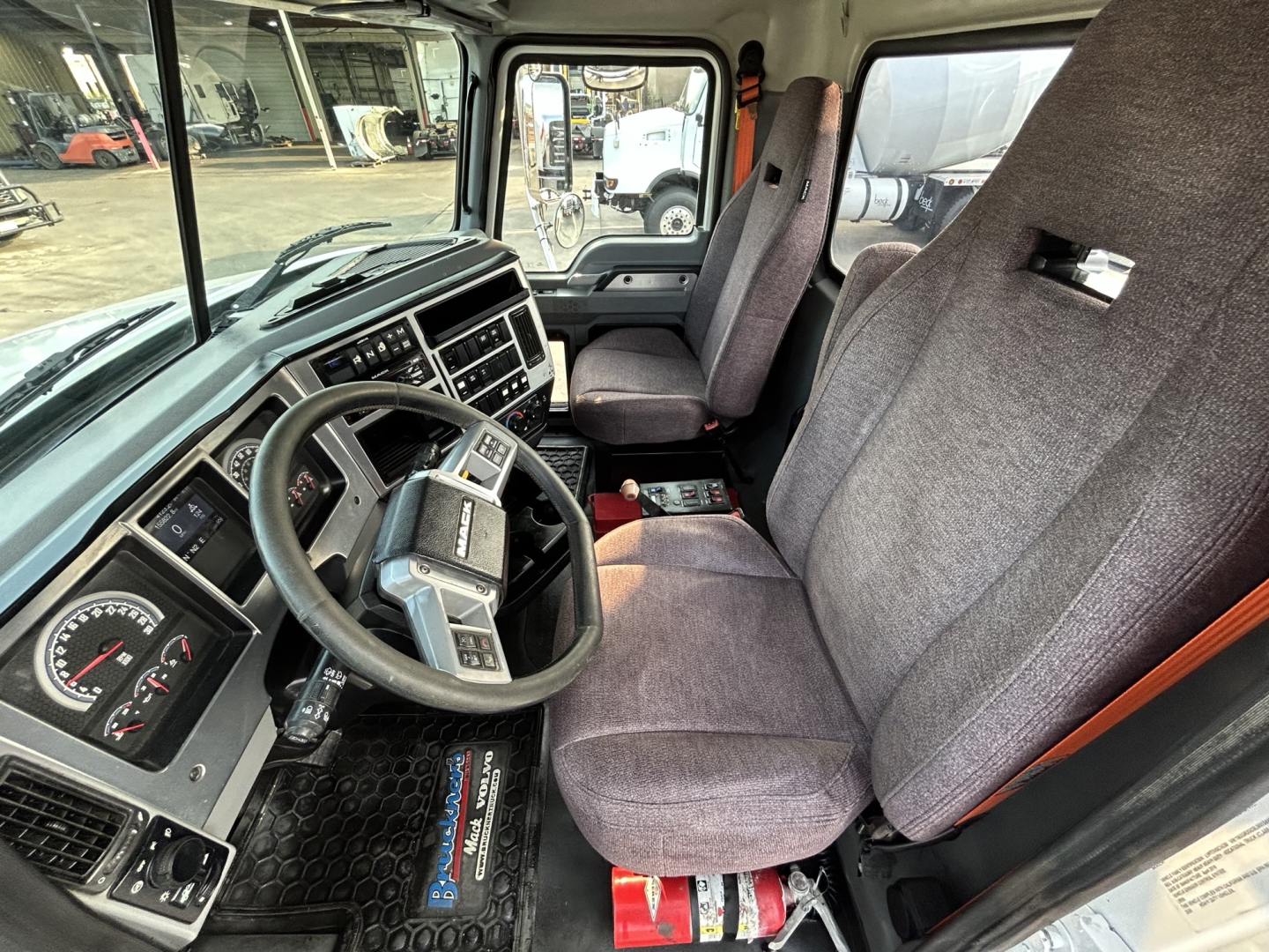 Cab interior of a 2020 Mack GR64B mixer truck showing steering wheel, gauges, and two front seats with fabric upholstery; dashboard with digital displays; center console; pedals; floor mat.