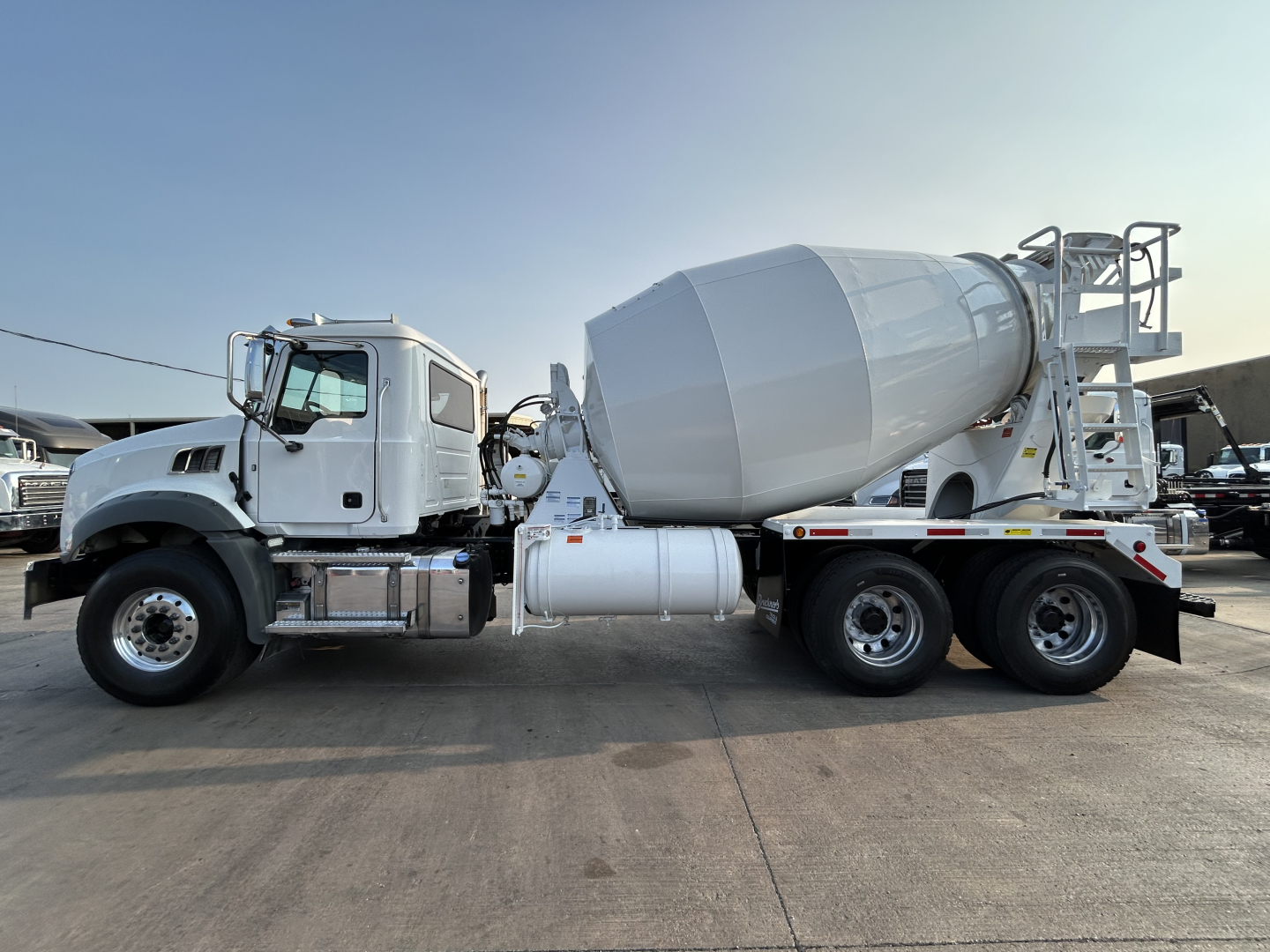 Mixer truck with a concrete mixer body and rotating drum on a Mack GR64B chassis side view showing the cement mixer and rear wheels.
