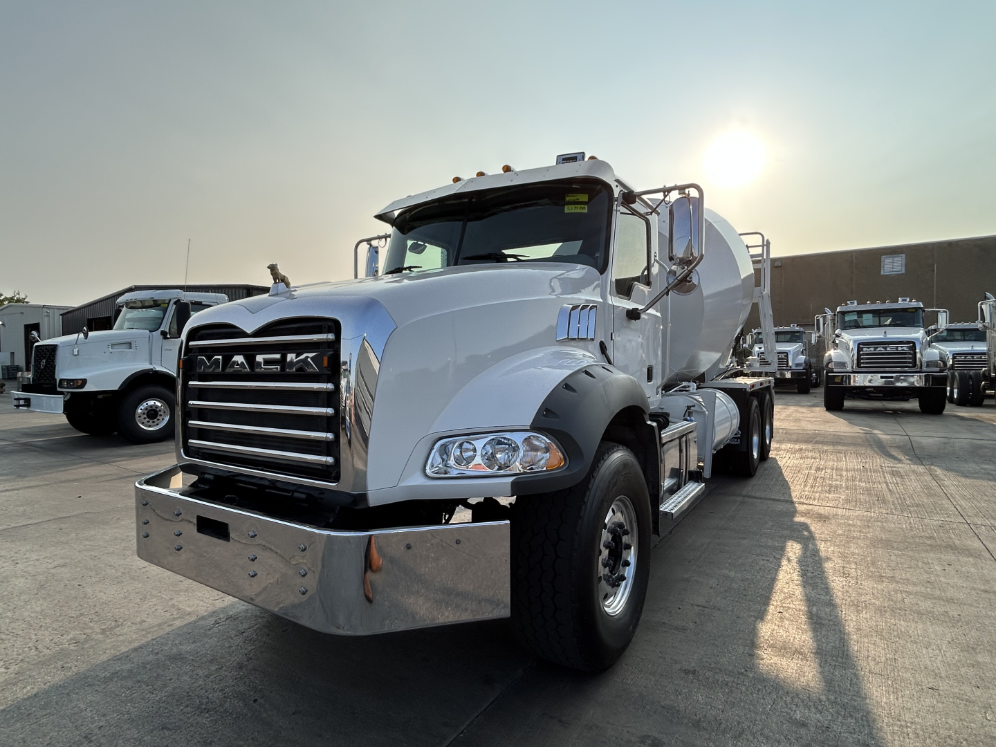 Front-left view of a white 2020 Mack GR64B mixer truck with large chrome grille, bumper, and headlights. The cab is white, with mirrors and step details visible; other trucks in background.