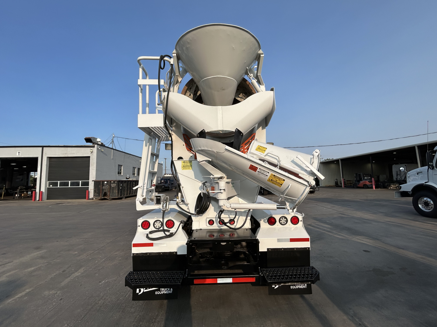 Mack GR64B mixer truck rear view showing cement mixer drum and chute, white with red reflective markings.