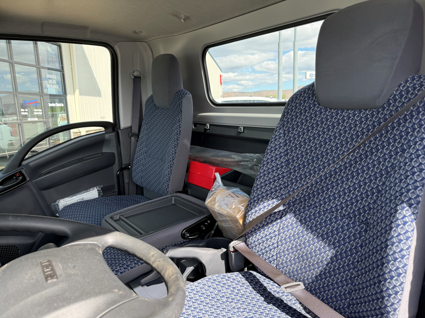 Isuzu NPRGASHD cab and chassis interior view with two fabric seats, dashboard, steering wheel, center console, and side window.
