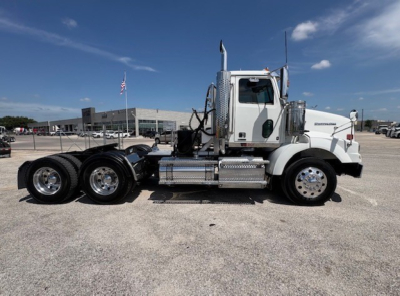 Western Star 4700SF daycab truck side view showing chrome fuel tanks and dual rear axles with triple tires, white cab, clear sky.