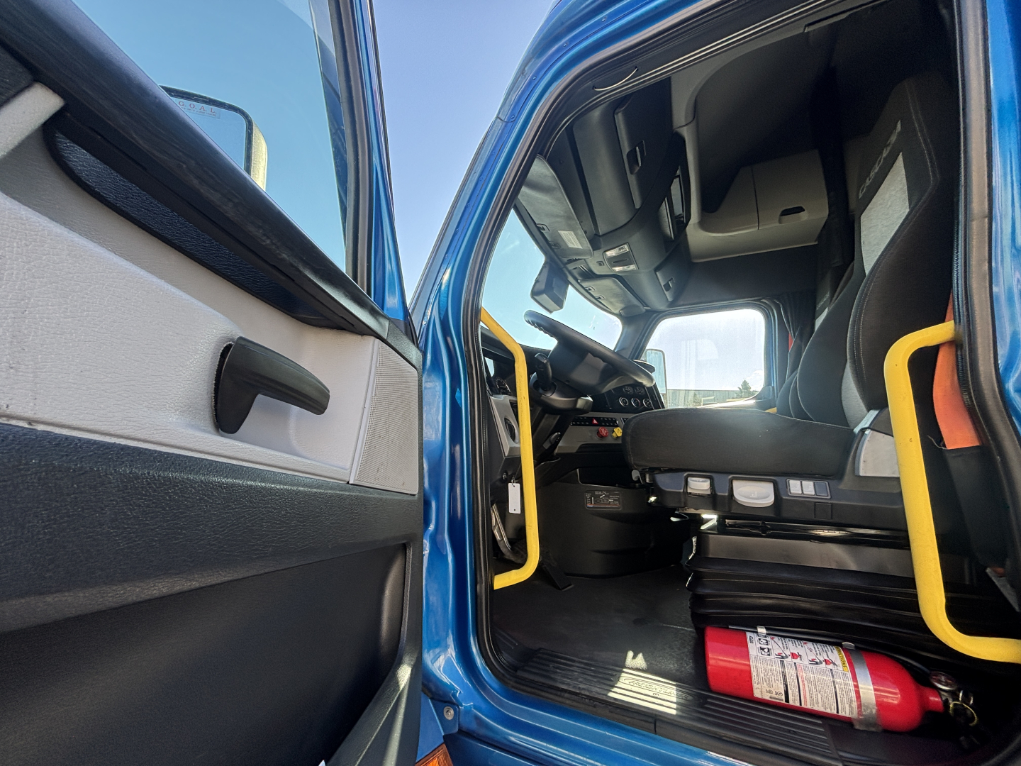 Freightliner PT126064ST truck cab interior view from open door showing driver seat, dashboard, steering wheel, and yellow grab rails.