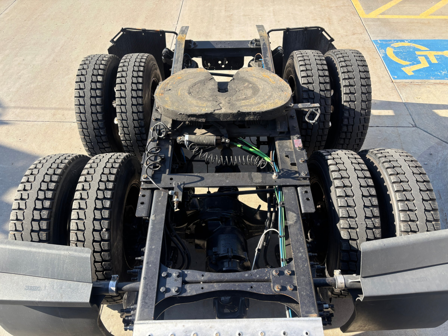 Truck chassis view showing rear dual-axle setup with six tires, fifth-wheel plate, and drivetrain components visible.