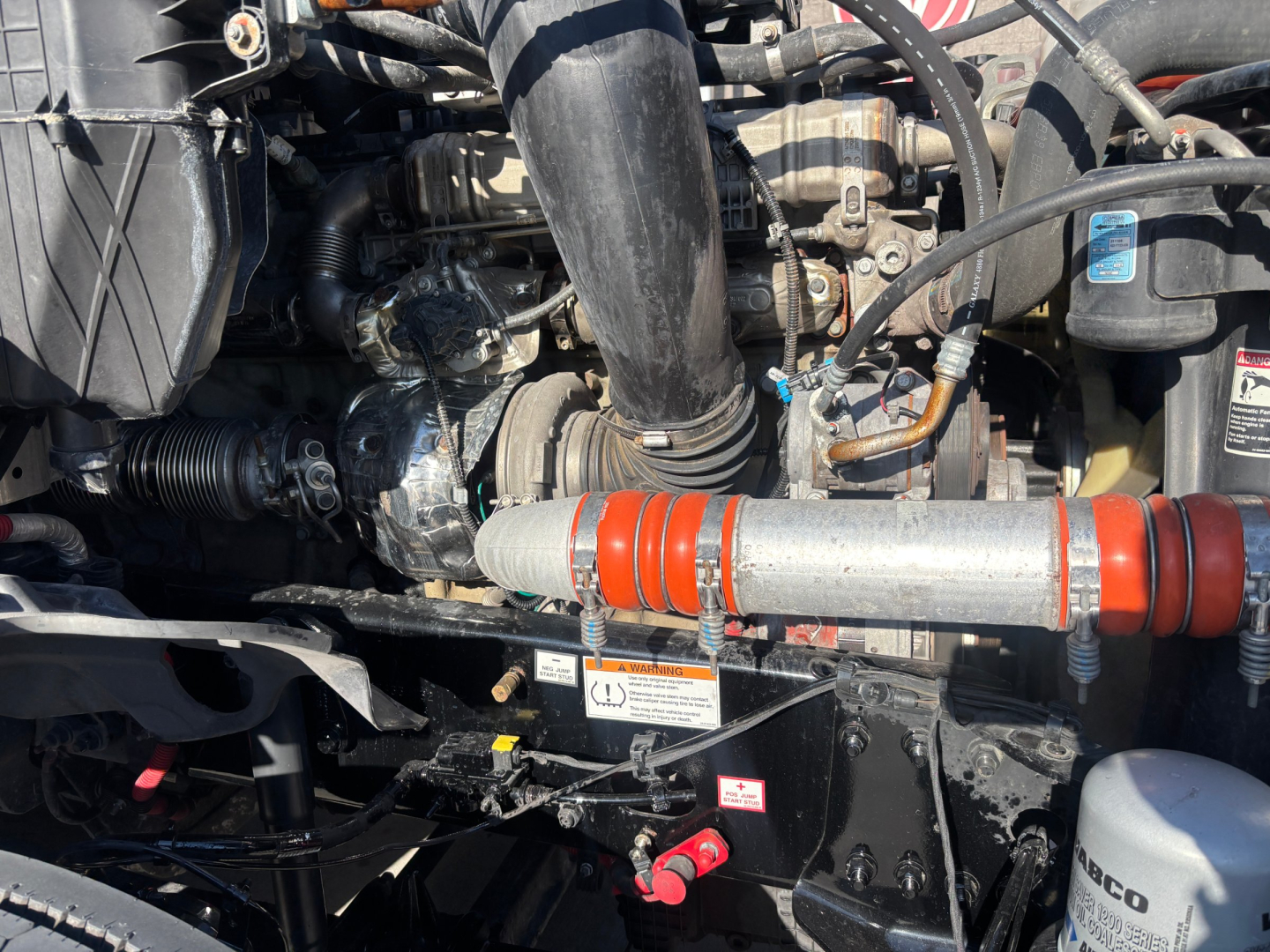 Engine bay of a Freightliner PT126064ST showing hoses, belts, and engine components with orange-red coolant hose and black intake piping.