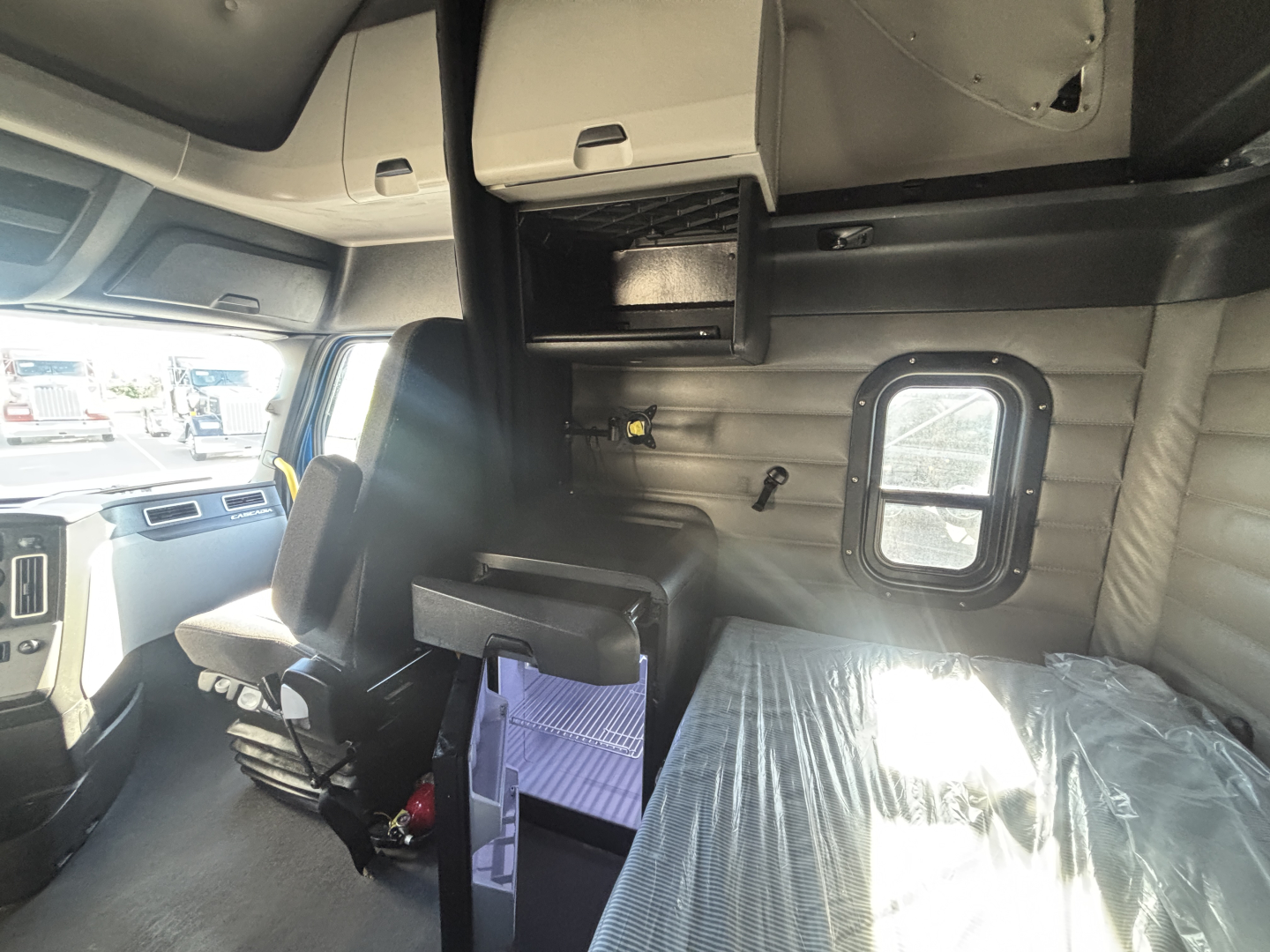 Cab interior of a Freightliner truck showing sleeper area with bunk and overhead compartments. Visible text includes no explicit labels in image; the surrounding vehicle interior captured.