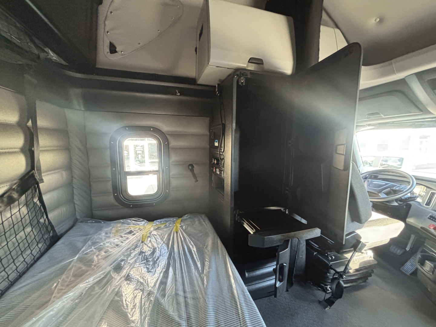Freightliner PT126064ST truck cab interior showing sleeper area with plastic-covered bed, storage cabinet, and driver seat area.