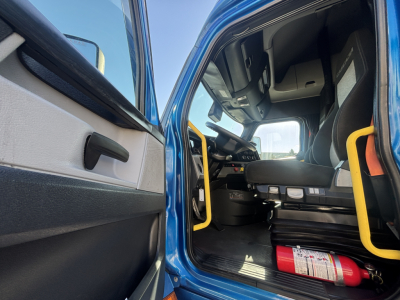 Freightliner PT126064ST truck cab interior view from open door showing driver seat, dashboard, steering wheel, and yellow grab rails.
