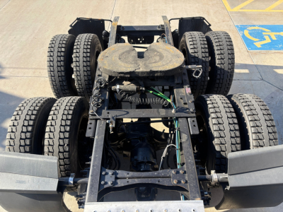 Truck chassis view showing rear dual-axle setup with six tires, fifth-wheel plate, and drivetrain components visible.