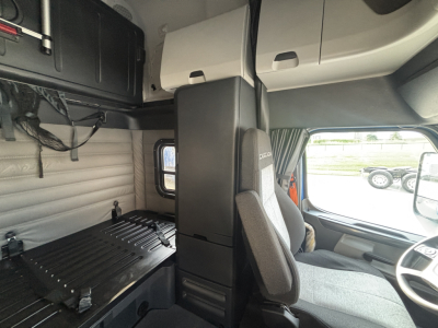 Interior sleeper cab of a Freightliner truck showing bunk area, storage shelves, and driver's seat with steering wheel visible.