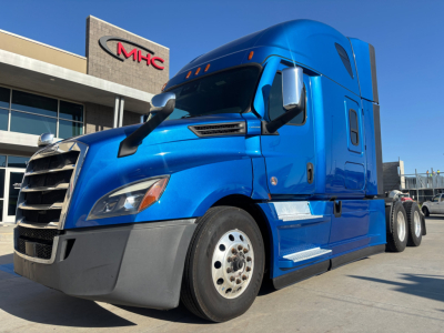 Truck shows a blue Freightliner PT126064ST tractor in a dealership lot with a modern cab and large front grille.