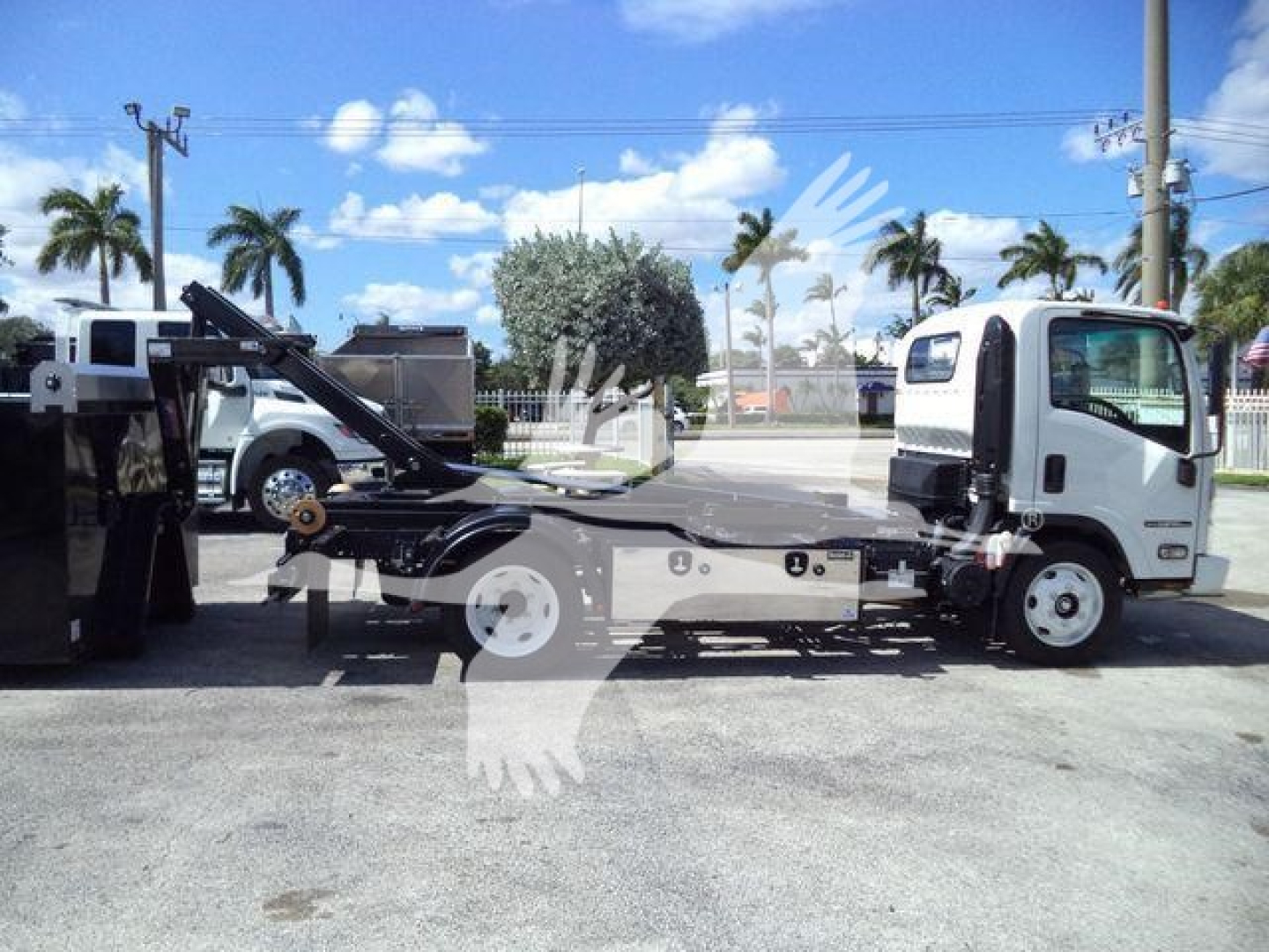 Isuzu NPR-HD tow truck with hooklift platform, side view showing cab and equipment, no visible legible text.