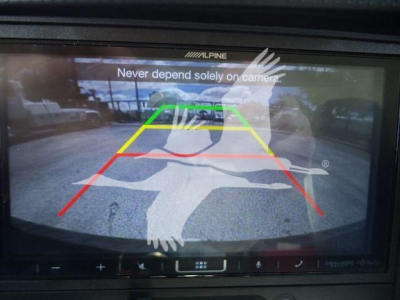 Isuzu NPR-HD truck rearview camera display showing backup guidelines and overlay logo.