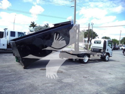 Isuzu NPR-HD hooklift truck with a large black dump bed tilted upward, white cab, and other trucks in the background.