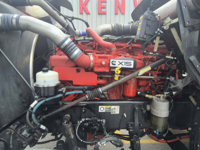 Kenworth W900L engine bay with red Cummins engine labeled 'AXIS' or 'AXIS' badge, hoses, and fluid reservoirs visible.