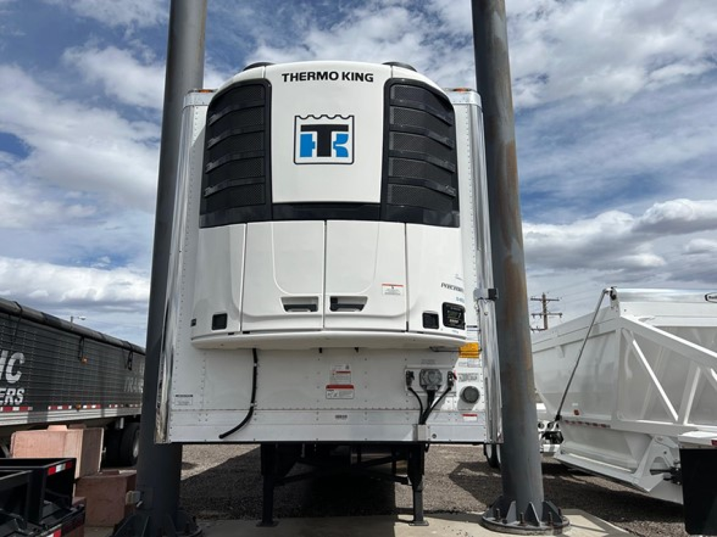 Thermo King unit mounted on front of white trailer refrigeration system with black vents and blue Thermo King logo; supporting legs and surrounding equipment.