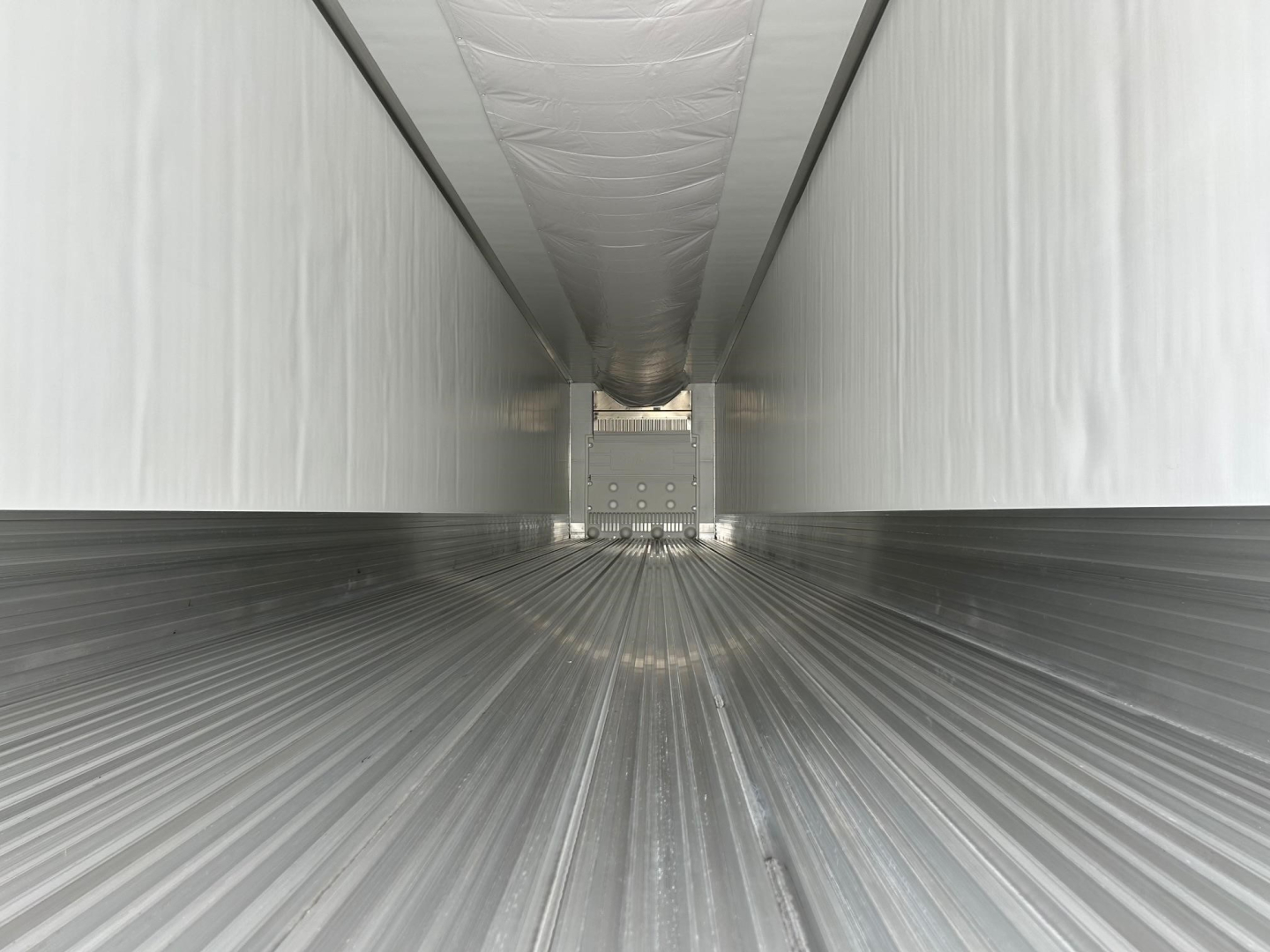 Trailer interior showing corrugated aluminum floor and vertical sidewalls with insulated ceiling along a long narrow corridor.
