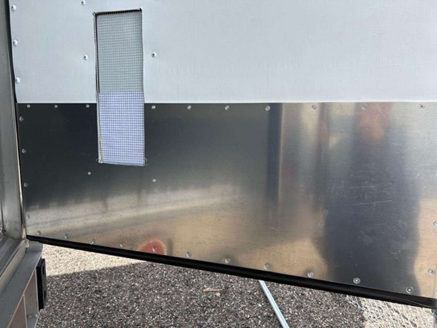 Trailer side panel with metal diamond-plate lower section and a small vertical rectangular vent or screen near top left.