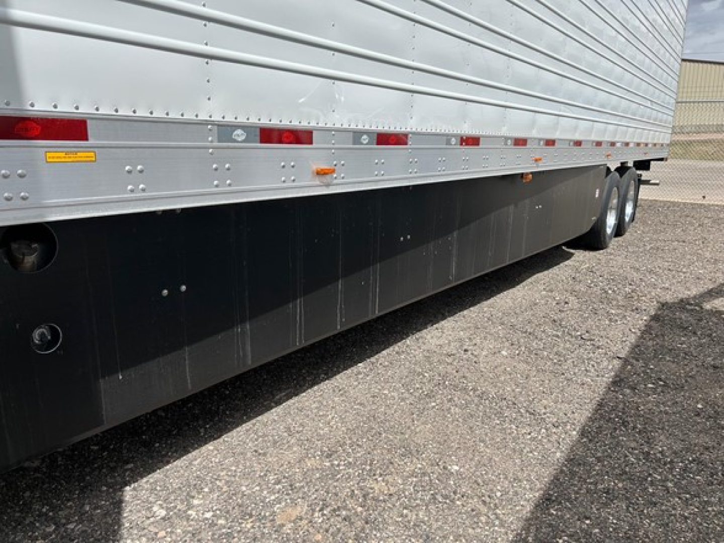 Trailer side view showing lower black skirts, silver corrugated side panel, undercarriage wheels, and reflective markers on a 2026 Utility 3000R trailer.