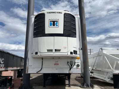 Thermo King unit mounted on front of white trailer refrigeration system with black vents and blue Thermo King logo; supporting legs and surrounding equipment.
