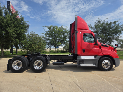 Side view of a red Freightliner PT126064S daycab truck on a concrete lot, showing chassis with dual rear axles and a raised sleeper cabin.
