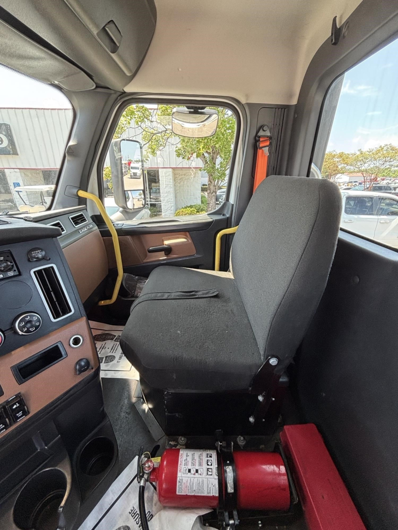 Cab interior of a Freightliner Cascadia 126 truck showing driver seat, dashboard, and a mounted fire extinguisher near the floor.