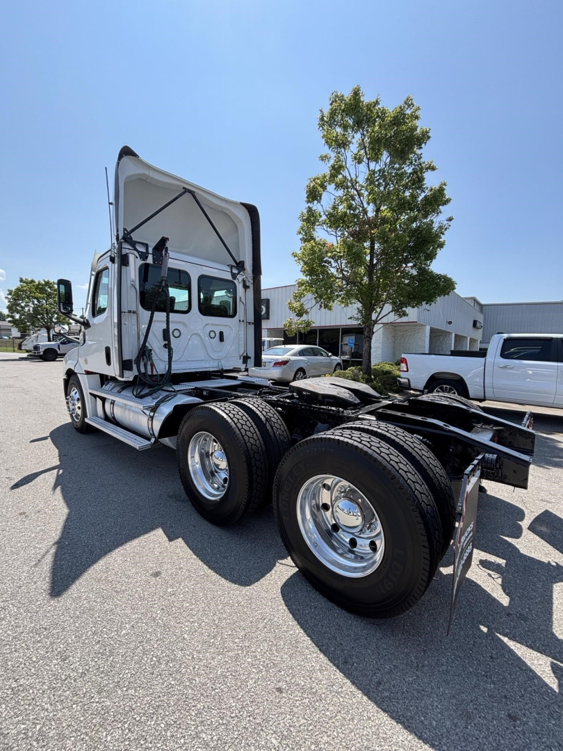 Freightliner Cascadia 126 day cab tractor rear three-quarter view with raised cab, dual rear axles, chrome wheels, and fuel tanks visible.