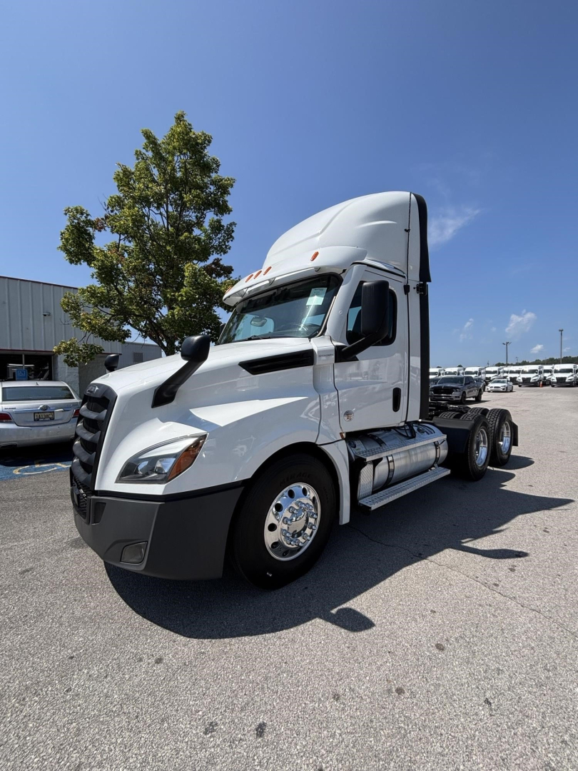 Freightliner Cascadia 126 day cab tractor in a parking lot, front-left view showing sleeper cab, white paint, chrome fuel tanks, and dual rear axles.