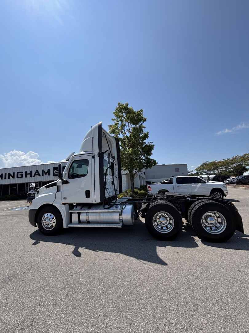 Side view of a white Freightliner Cascadia 126 day cab tractor, showing fuel tanks and rear axle configuration.