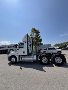 Side view of a white Freightliner Cascadia 126 day cab tractor, showing fuel tanks and rear axle configuration.