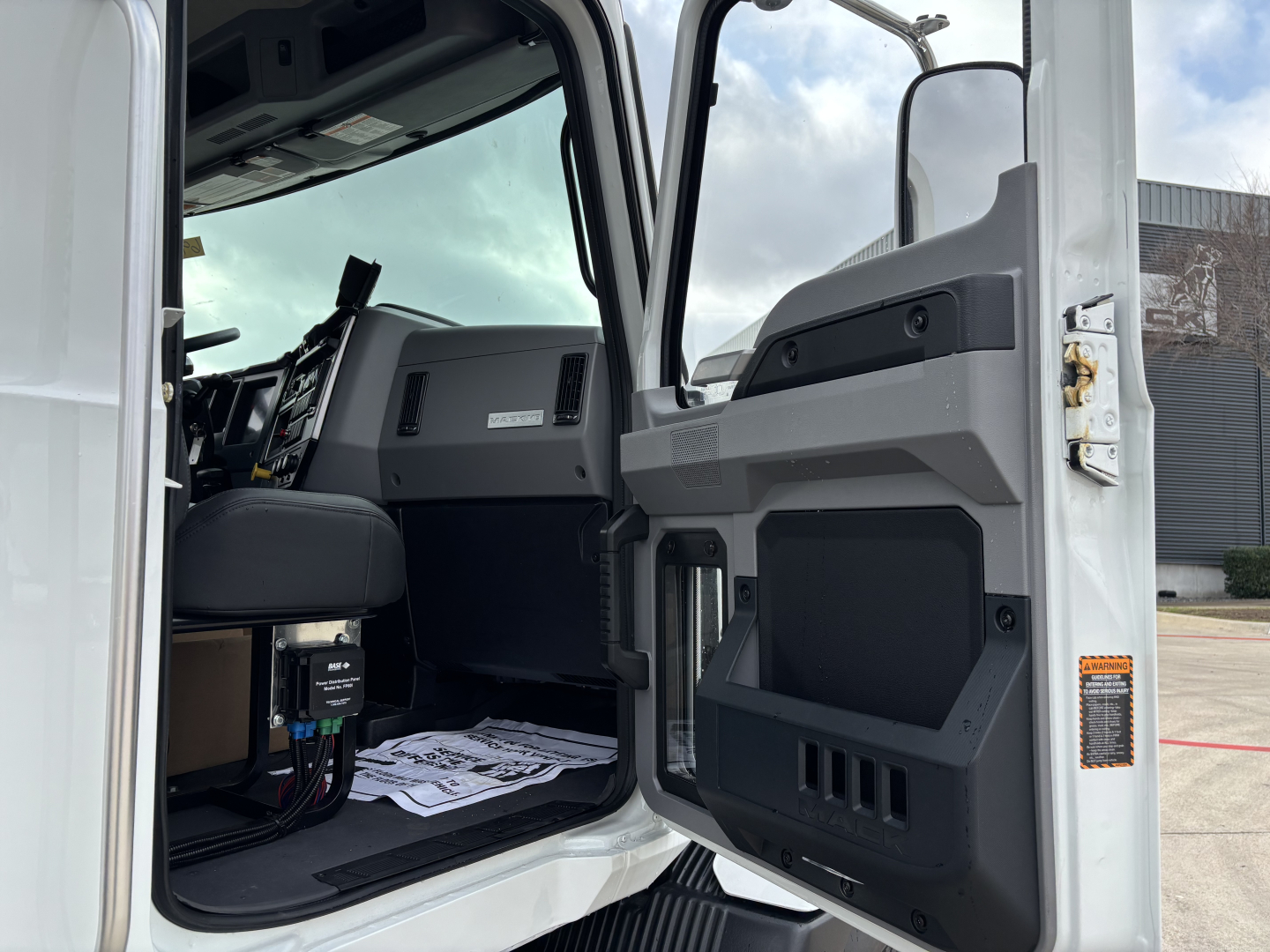 Truck cab interior door panel view of a 2026 Mack MD7 showing driver seat and dashboard area.