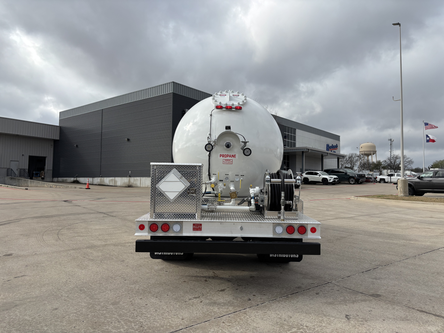 Rear view of a Mack MD7 tractor with a large cylindrical tank trailer attached, in a dealership lot.