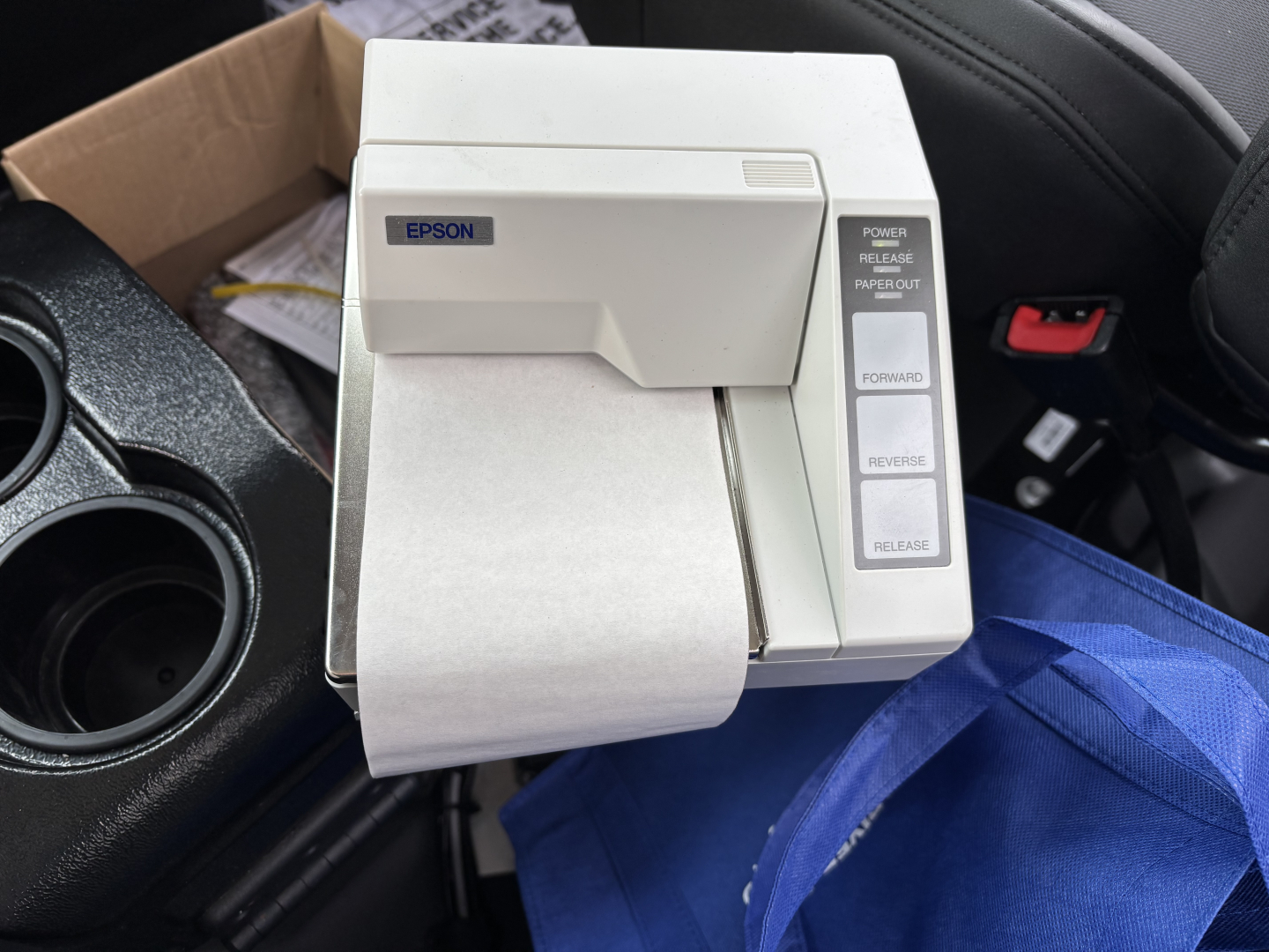 Epson receipt printer in vehicle cabin with paper feed and control buttons; visible text includes EPSON on label and buttons: POWER, RELEASE, PAPER OUT, FORWARD, REVERSE, HOLD/RELEASE.
